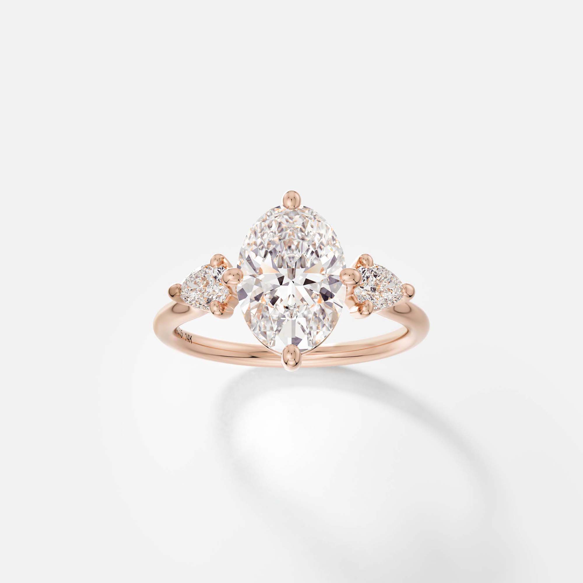 14k rose gold three stone engagement ring with 2 carat oval diamond and pear side stones on delicate round profile band