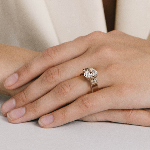 close view of oval diamond three stone ring with baguette side stones in partial bezel on flat band