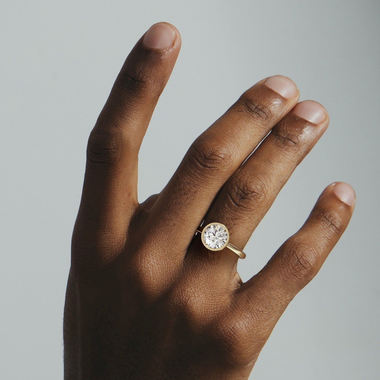 Syd round brilliant diamond bezel engagement ring worn on hand