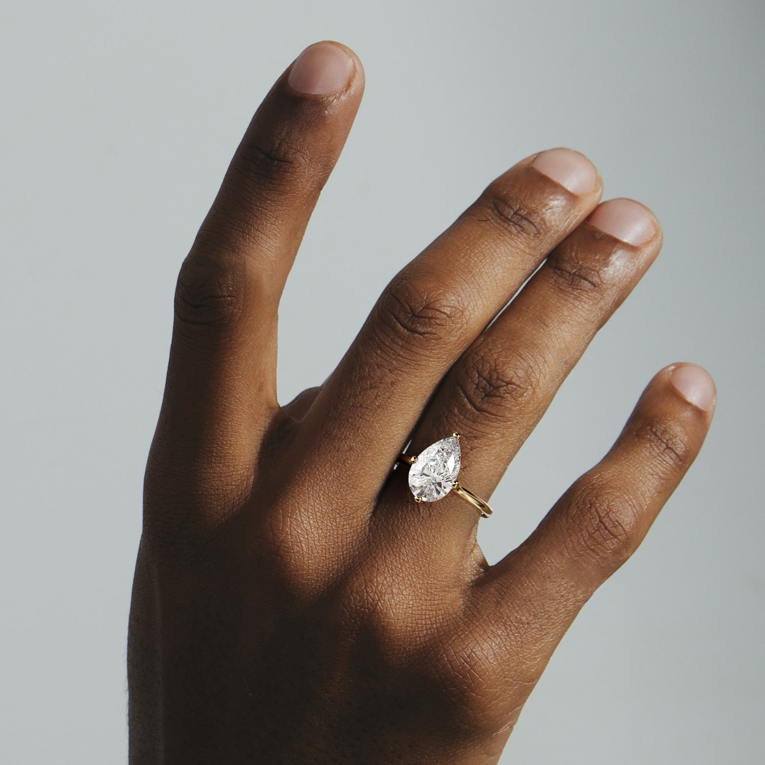 Dainty yellow gold engagement ring with pear diamond worn on hand