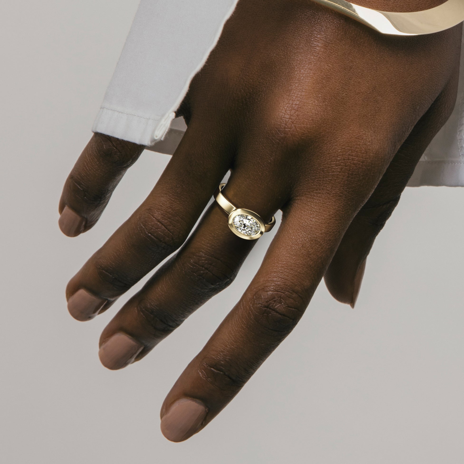 Close view of oval diamond set east west in thick bezel on sculptural wide band