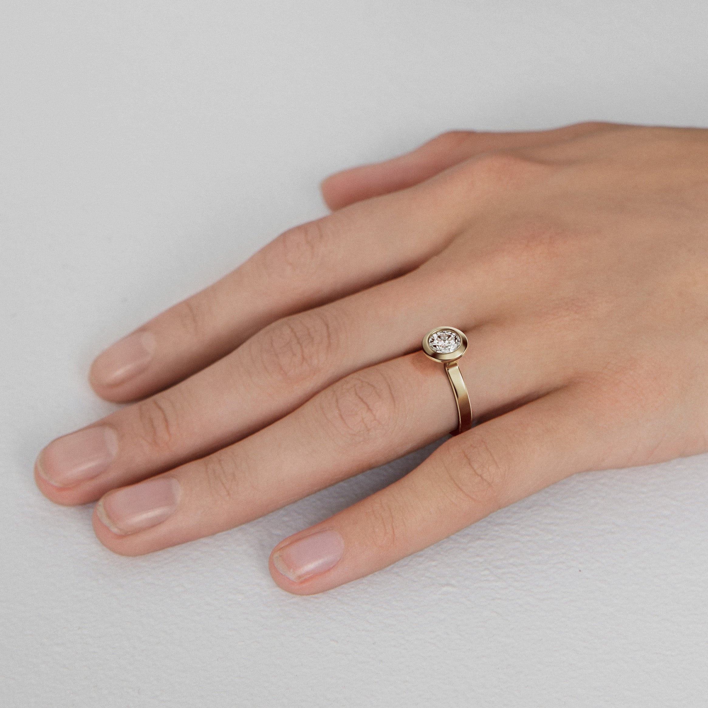 Close view of round brilliant diamond in thick bezel on sculptural flat band