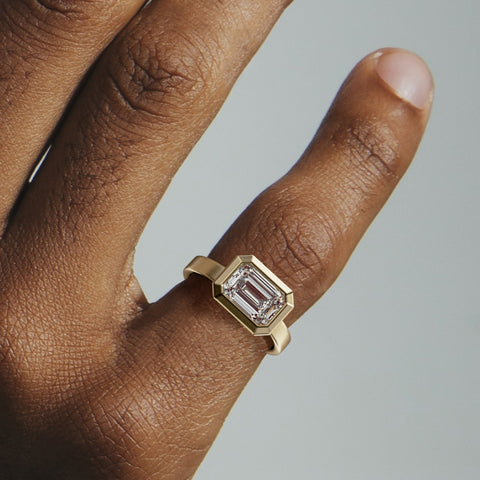 Close view of emerald-cut diamond set east west in thick bezel on wide flat band