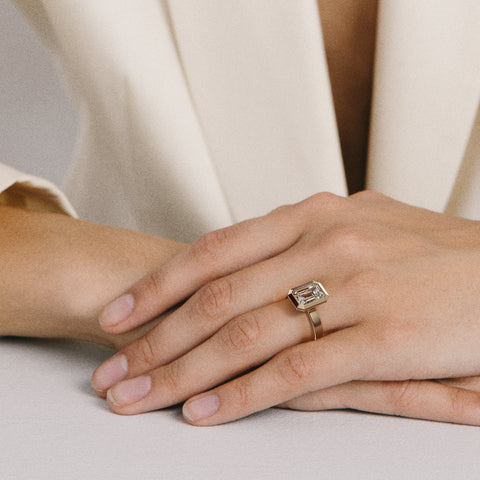 Close view of emerald-cut diamond set north south in thick bezel on wide flat band