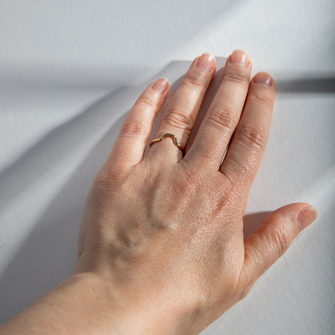 Thin round gold ring with curved detail worn on hand