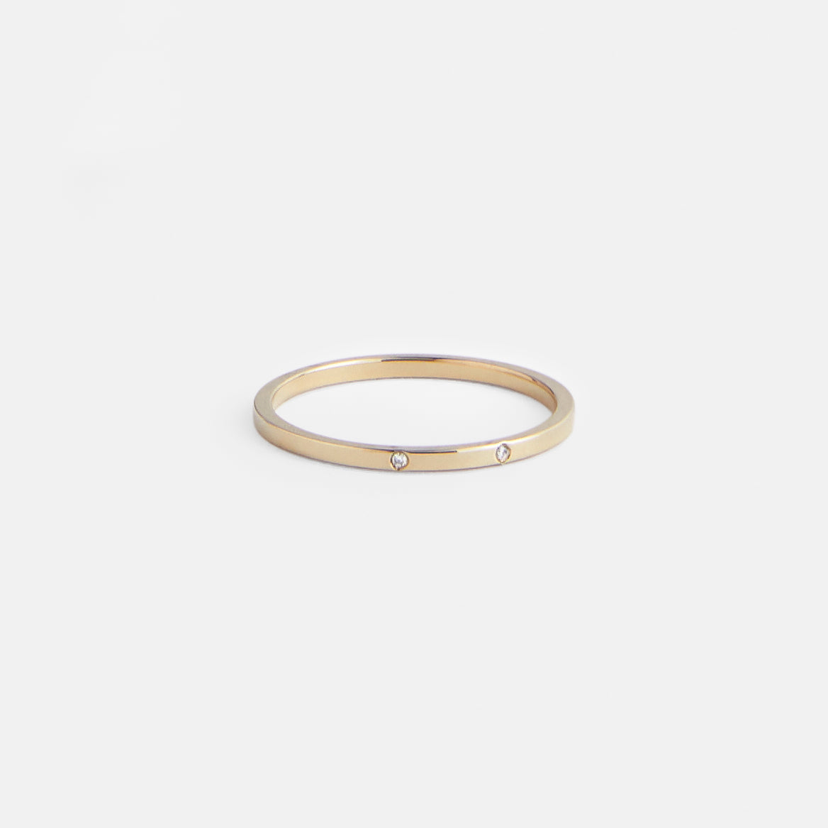 Thin flat gold wedding band with two round brilliant diamonds worn on hand